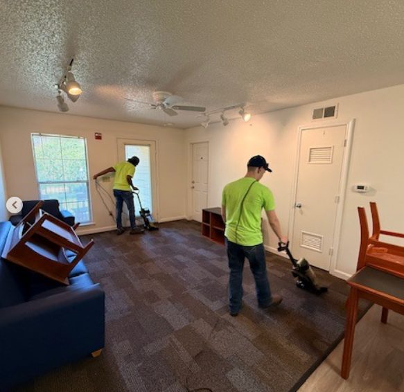 Two team members vacuuming carpet in an apartment